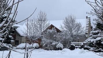 Un paysage enneigé avec une cabane en bois, des arbres sans feuilles et une voiture recouverte de neige.