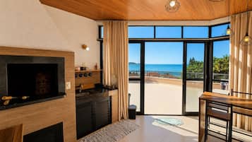 Una cocina moderna con estufa integrada, un comedor con mesa y sillas, y un amplio ventanal corredero que da a un balcón con vistas al mar.