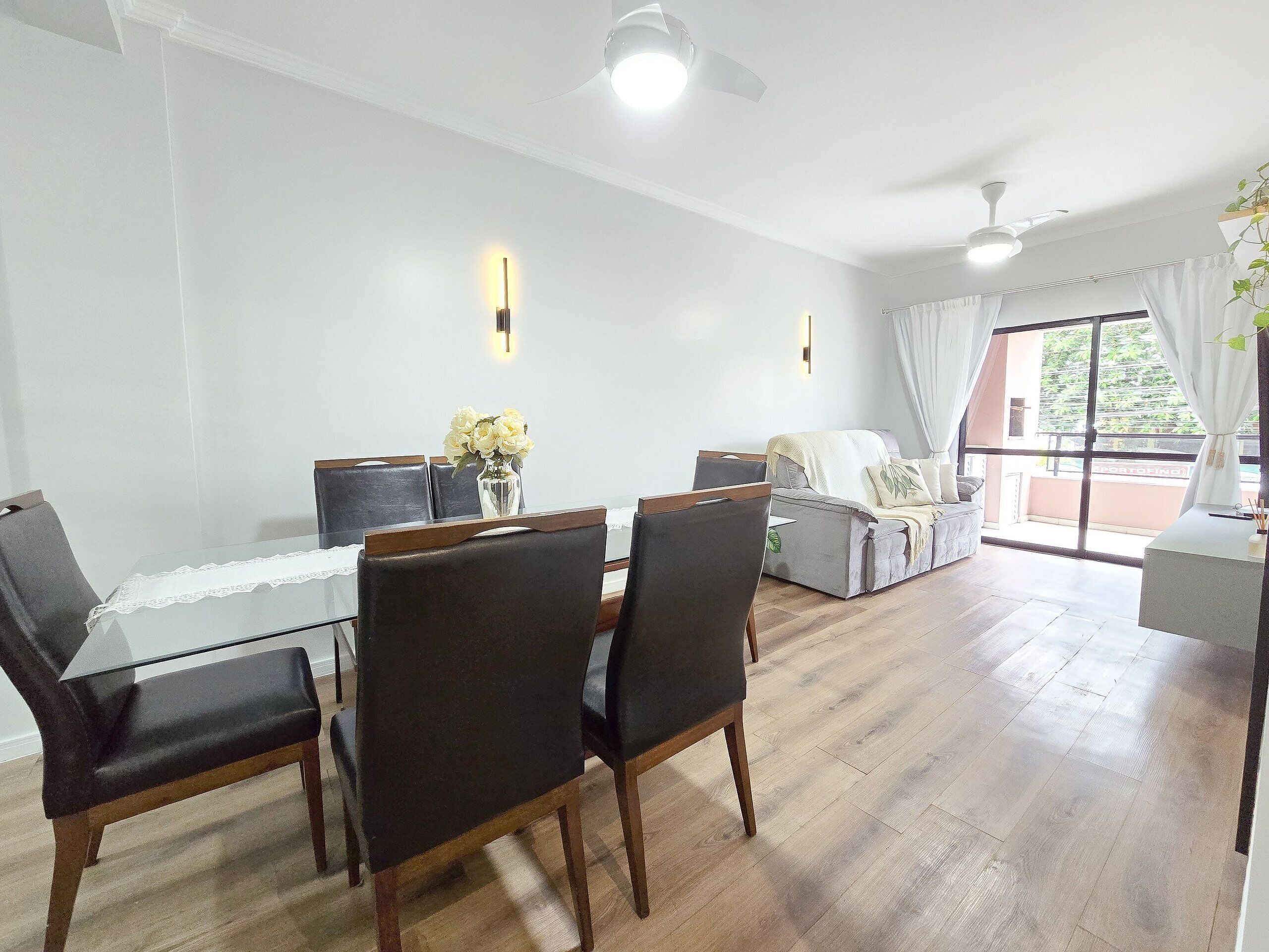 A dining area with a glass table and chairs, a sofa, and a view of the outdoors through a sliding door.