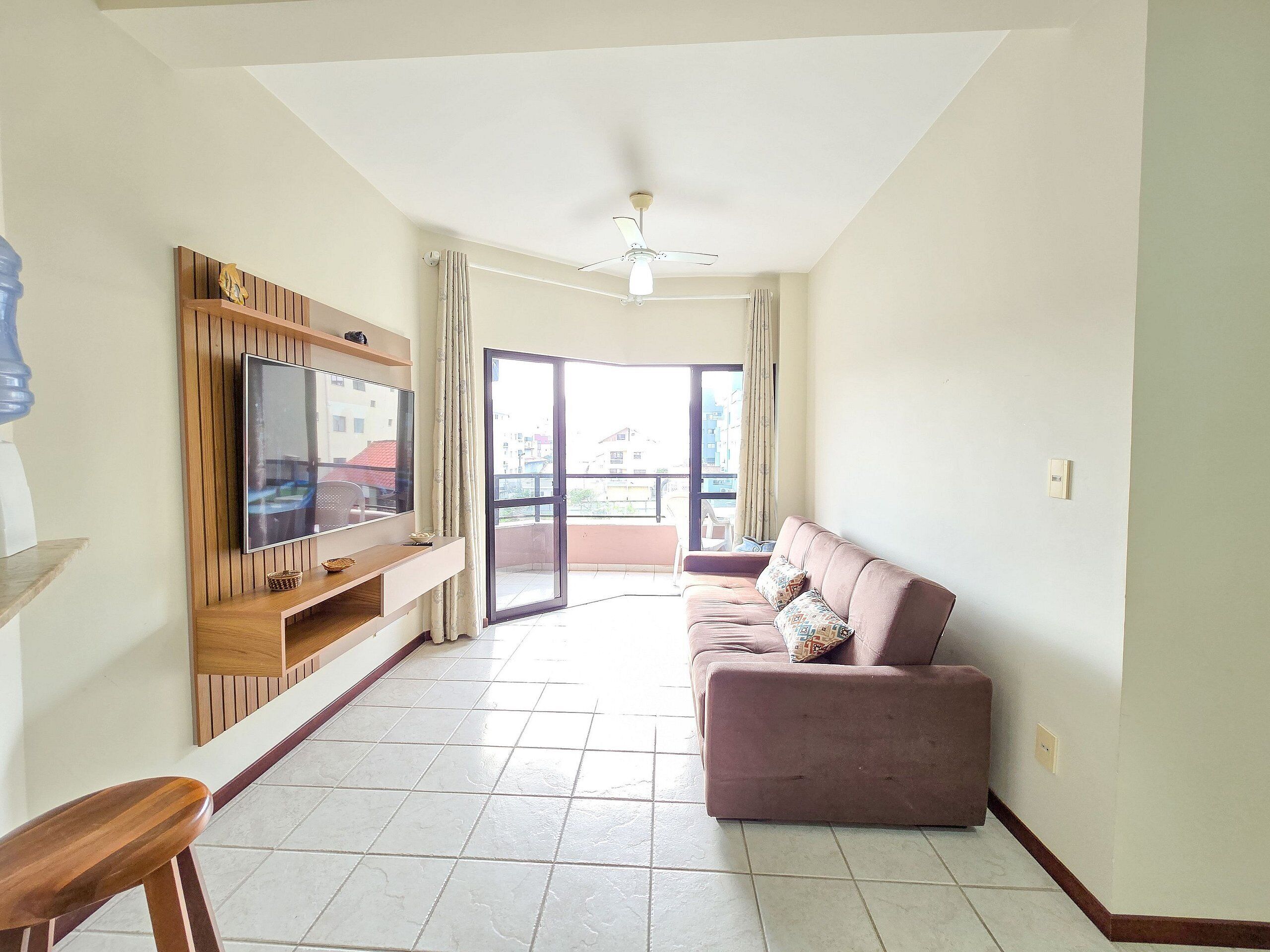 A living room with a flat-screen TV, a sofa, and a balcony with a view of buildings.