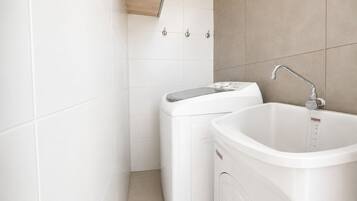 A bathroom with a washing machine, a sink, and a shower.