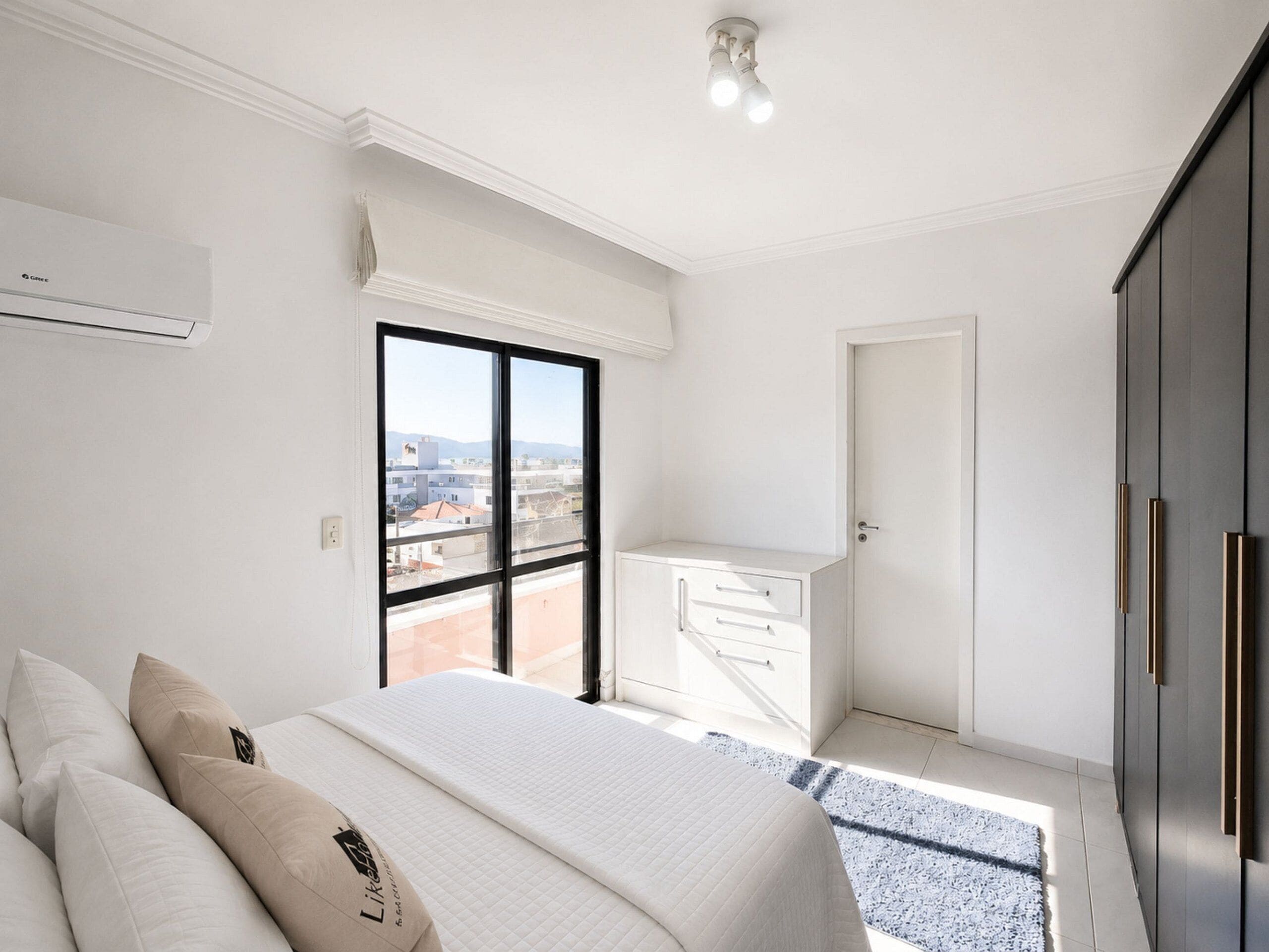 A modern bedroom with a large bed, a view of the city through a window, and a balcony.