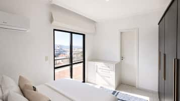 A modern bedroom with a large bed, a view of the city through a window, and a balcony.
