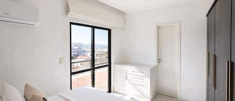 A modern bedroom with a large bed, a view of the city through a window, and a balcony.