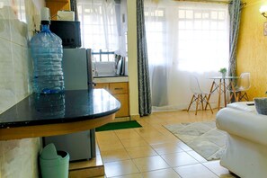A kitchen with a water dispenser, a microwave, and a sink. There is a dining area with a chair and a table. - Cijana Gardens - School lane 1 br Westlands (Nairobi)