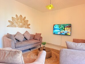 A living room with a sofa, armchairs, a coffee table, a wall art piece, and a television. - Mamelles Beachside Retreat  (Dakar)