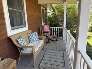 A wooden porch with a wicker sofa, rocking chair, and a patterned rug.
