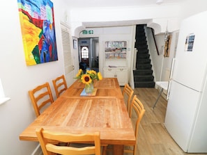 Ein Essbereich mit Holztisch, Stühlen, einer Vase mit Sonnenblumen, einem Bücherregal mit DVDs und einer Treppe.