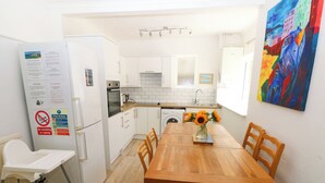 A compact kitchen with white cabinets, a wooden dining table, and a white chair. - 3 Edward Street (Tenby)