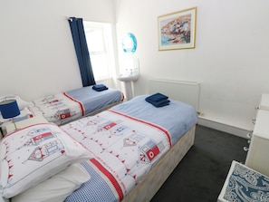 Ein Hotelzimmer mit zwei Betten, einem Fenster mit Vorhängen, einem Waschbecken, einem Heizkörper und einem Bild an der Wand.