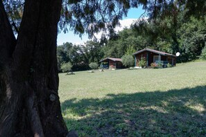 A rustic cabin with a red roof, surrounded by a grassy field and dense trees. - Chalet 'D'alpion' with Shared Pool, Private Terrace and Shared Garden (Les Tourrettes)