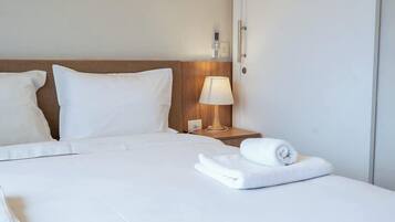 A hotel room with a neatly made bed, a bedside lamp, and a rolled towel on the bed.
