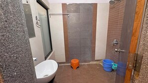 Ein kleines Badezimmer mit einem weißen Waschbecken, einer Duschkabine aus Glas, einer Holztür und einem gefliesten Boden.