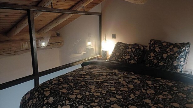 Un dormitorio con techo de madera, una cama con colcha estampada, una mesita de noche con lámpara y una ventana con vistas.