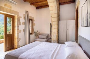 A bedroom with a large bed, a wooden ceiling, stone walls, a wardrobe, and a view of greenery outside. - Dream View Villa Kastellos (Kastellos)