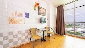A room with a dining table and chairs, a TV, and a large window with a view of buildings. - Collection O Thanh Van Hotel - Binh Tan (Ho Chi Minh City)