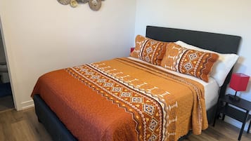 A bed with a patterned blanket and pillows, a bedside table with a lamp, and a wall decoration.