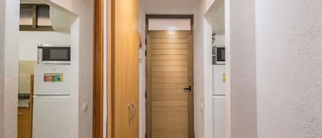 Un corridoio stretto con una porta in legno, un forno a microonde e un frigorifero a sinistra.