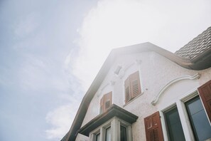 Un edificio con techo inclinado, una ventana con contraventanas y una esquina con moldura decorativa.