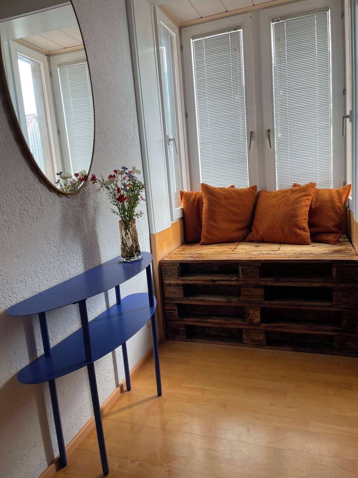 Une pièce avec un banc en bois, une table bleue et un miroir au mur.