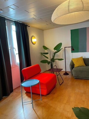 Een moderne woonkamer met een rode bank, een klein rond tafeltje, een vloerlamp en een grote potplant.
