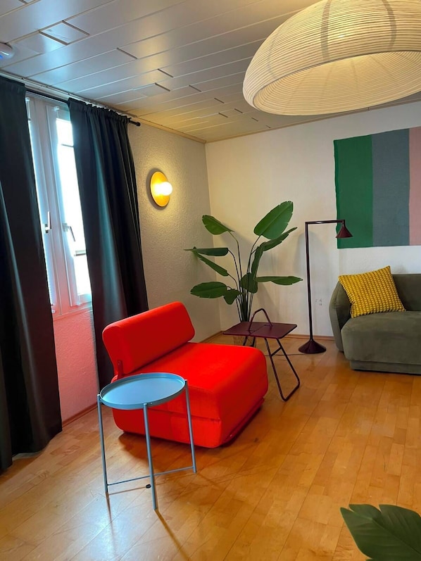A modern living room with a red sofa, a small round table, a floor lamp, and a large potted plant. - Villa Limoncello (Hard)