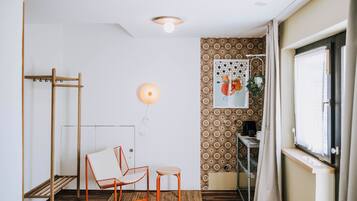 A room with a wooden floor, a metal chair, a small table, a wall-mounted light fixture, and a patterned wall.
