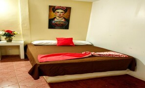 A single bed with a brown bedspread and a red pillow, a small bedside table with a vase of flowers, and a painting on the wall.