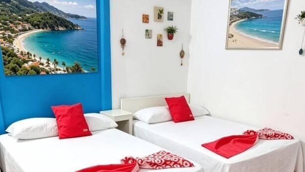 A hotel room with two beds, red and white bedding, a beach view painting, and a small wall decoration. - Hotel Zihua Malibu (Zihuatanejo)