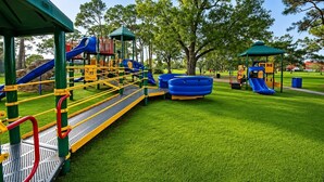A playground with slides and climbing structures, surrounded by grass and trees. - Restoration Hardware Home on PGA National Golf Course with Salt Water Pool (Palm Beach Gardens)