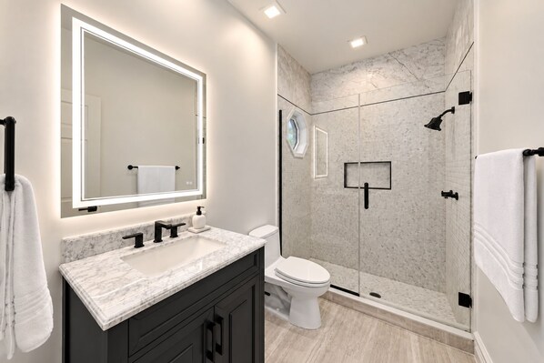 Une salle de bain moderne avec un grand miroir, un lavabo en marbre, des toilettes et une douche à parois de verre.
