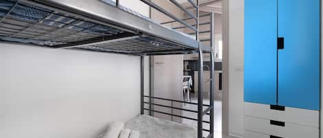 A bunk bed with a metal frame, a small table with a chair, and a blue wardrobe.