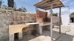An outdoor barbecue area with a brick oven, a concrete counter, and a metal roof structure.