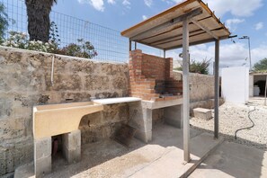 An outdoor barbecue area with a brick oven, a concrete counter, and a metal roof structure.