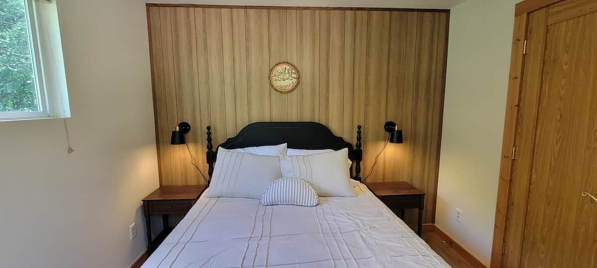 Ein Bett mit Kopfteil, zwei Nachttische mit Lampen und eine an der Wand hängende Uhr.