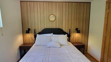 Ein Bett mit Kopfteil, zwei Nachttische mit Lampen und eine an der Wand hängende Uhr.