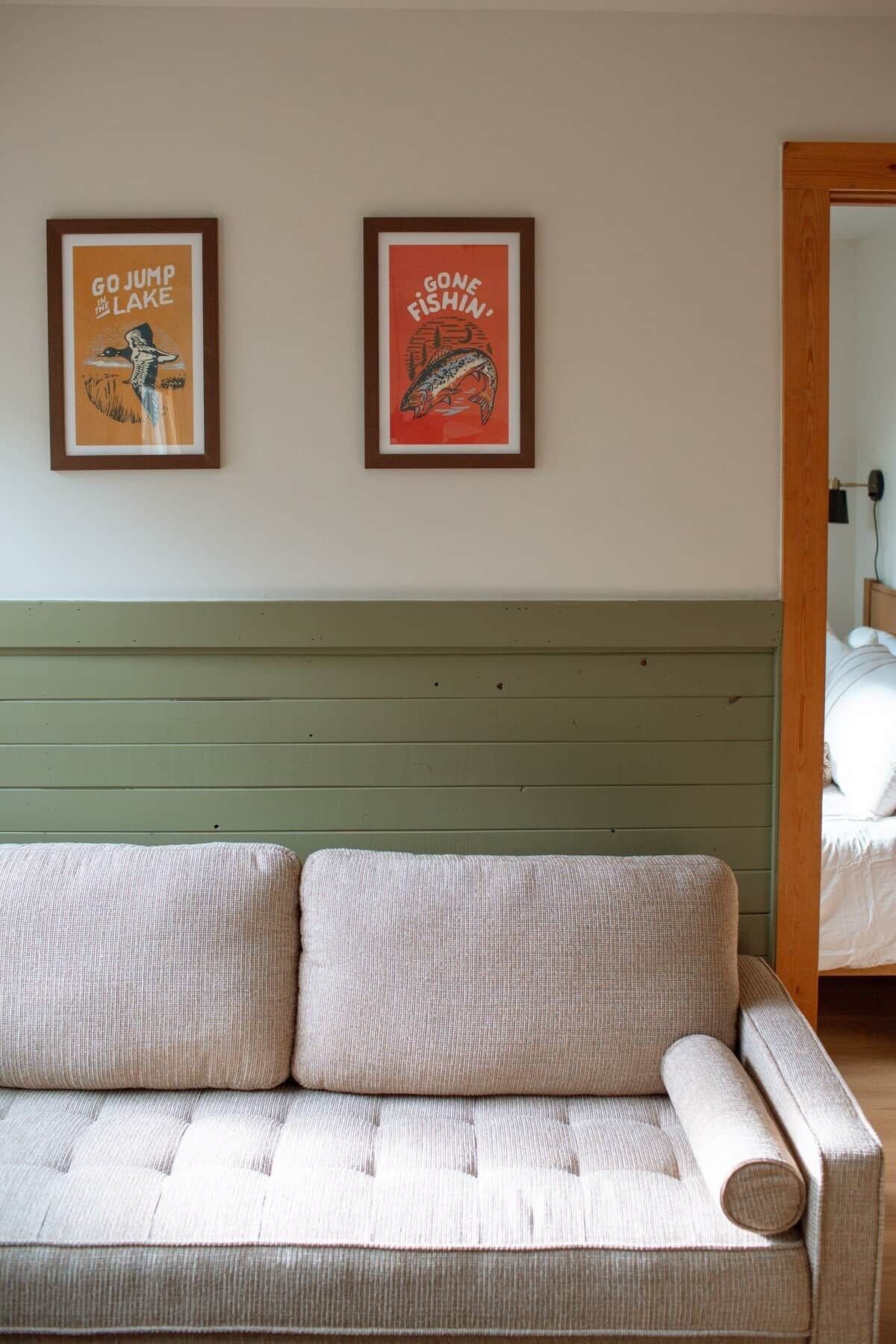 A room with a green upholstered sofa and two framed posters on the wall.