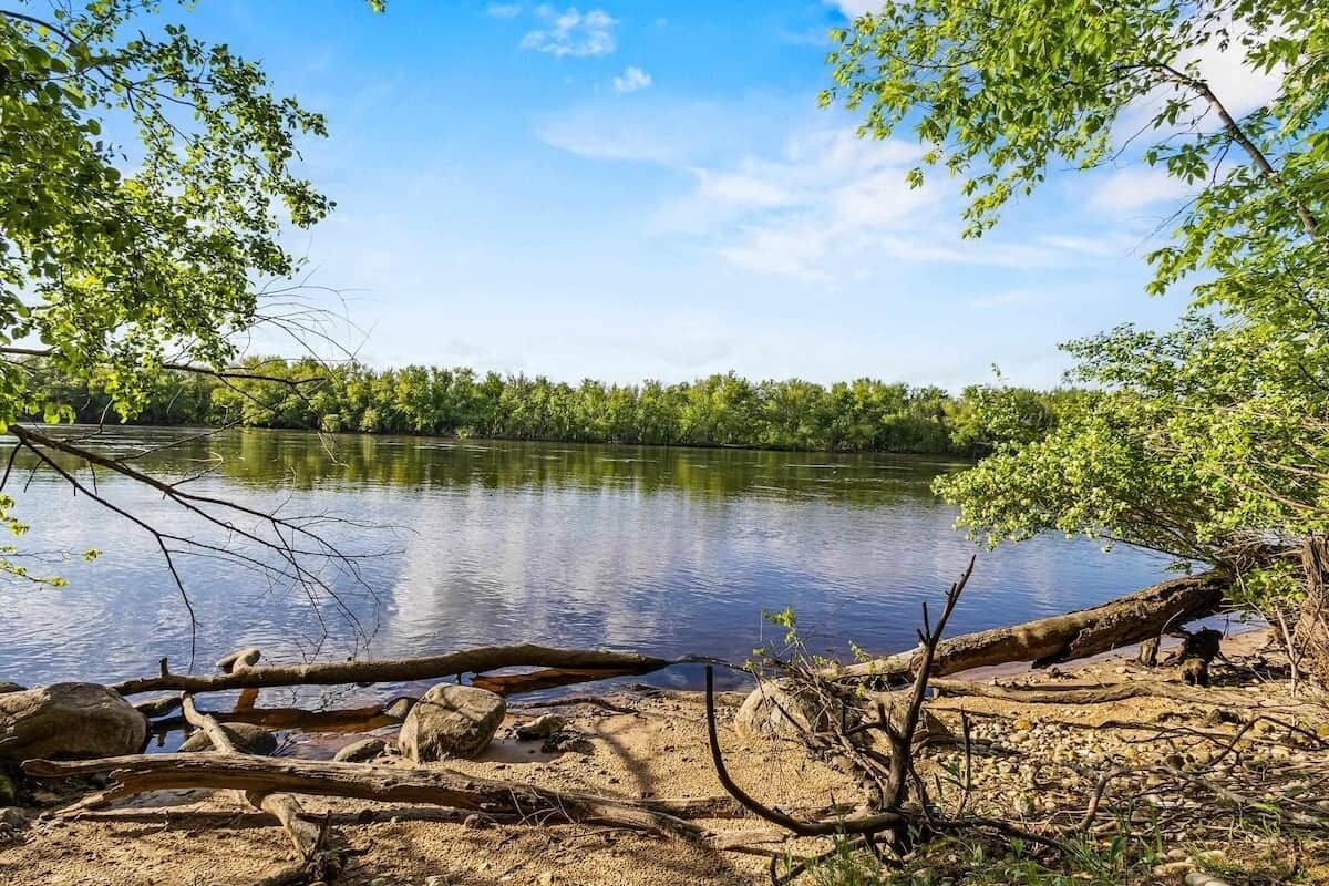Un paysage naturel avec un lac paisible, entouré d’arbres et bordé d’une plage de sable.