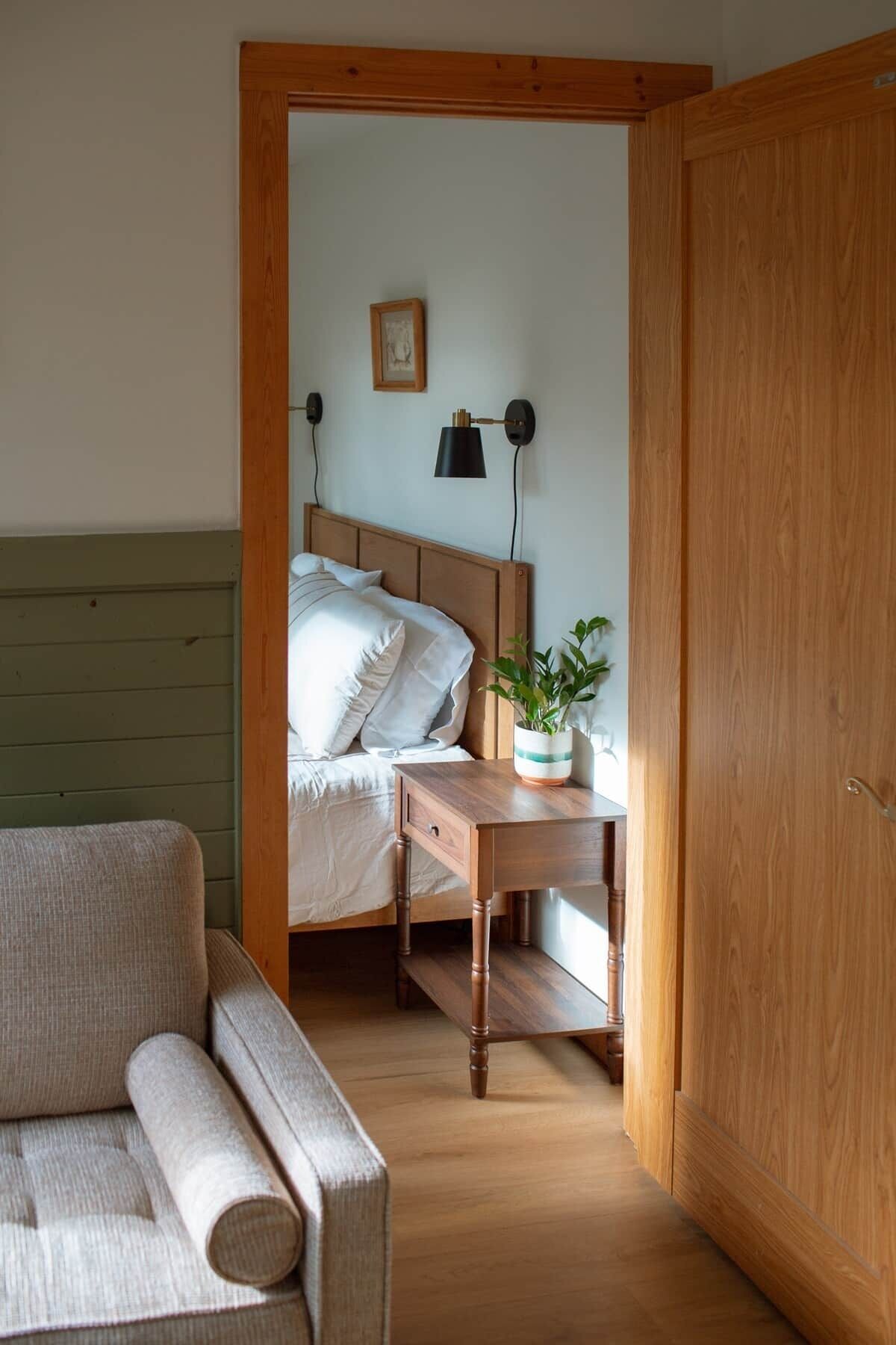 A bedroom with a bed, bedside table, lamp, and a chair.