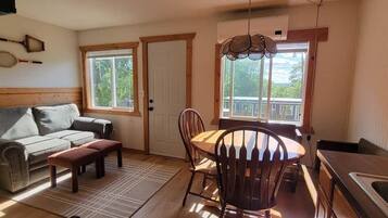 A cozy living room with a sofa, a dining table with chairs, a bench, and a kitchen area with a sink and a window.