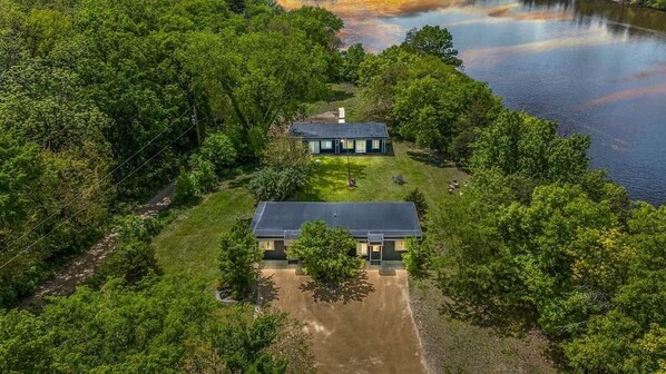 A two-story house with a large front lawn and a body of water in the background.