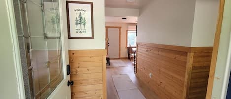 A hallway with wooden paneling, a framed welcome sign, and a door leading to a room.