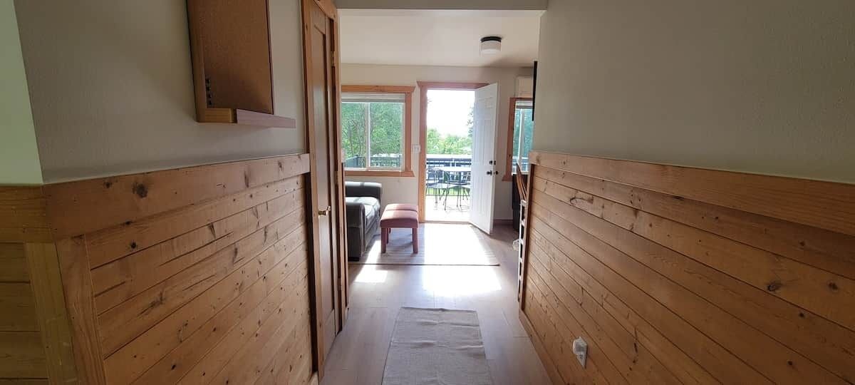 A narrow hallway with wooden paneling, leading to a room with a sofa and a table.
