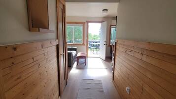 A narrow hallway with wooden paneling, leading to a room with a sofa and a table.