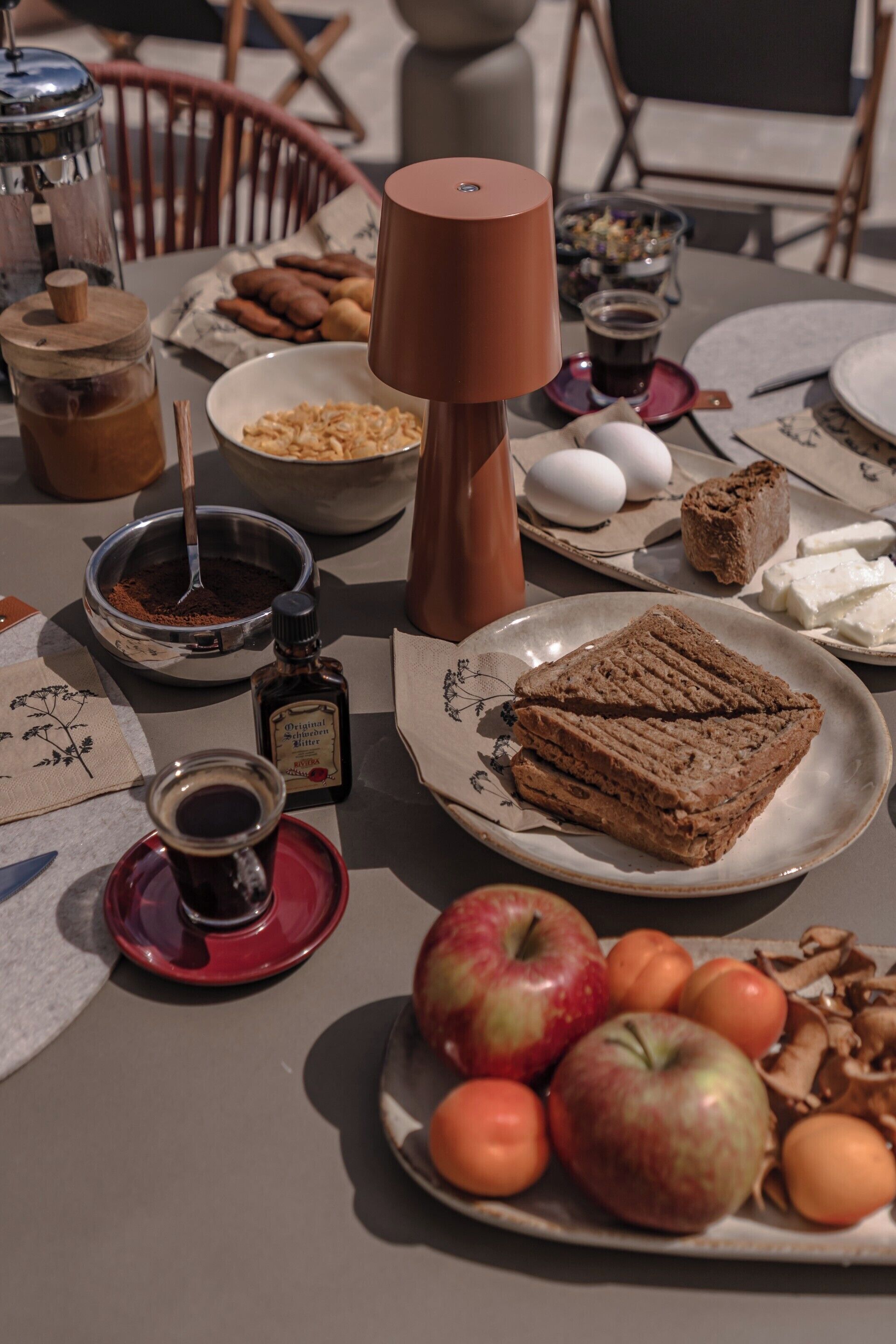 Una mesa dispuesta con alimentos como pan, huevos, manzanas y una botella de bebida.