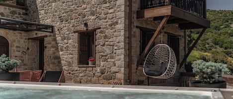 A stone building with a pool, outdoor seating, and a hanging chair.
