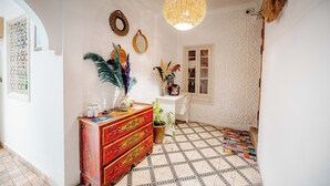 A hallway with a patterned floor, a red wooden dresser, a hanging woven light fixture, and decorative wall art. - Riad Green Vines (Marrakech)