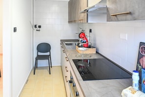 A compact kitchen with a black stovetop, a red coffee machine, and a single chair. - Appartamenti Saerre (Buonalbergo)
