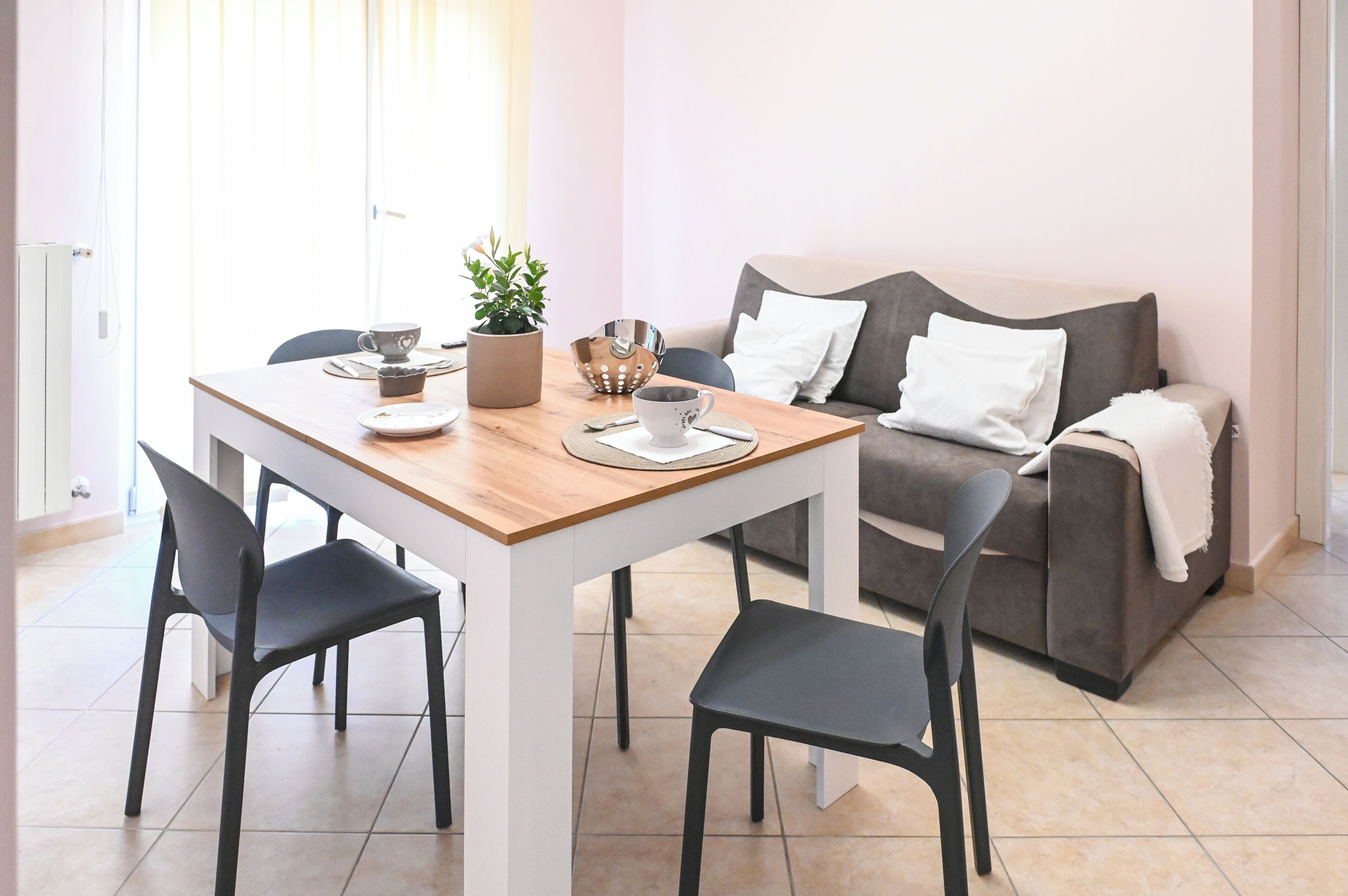 A modern living room with a dining table, two chairs, a grey sofa, and a potted plant.