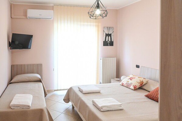 A hotel room with two beds, a flat-screen TV, a radiator, and a window with curtains.